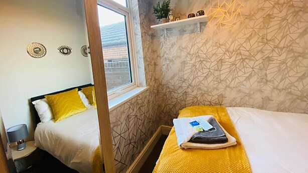 A hotel room with two beds, a window, a geometric-patterned wall, and a shelf with decorative items. - Townhouse @ 110 Etruria Vale Road Stoke (Stoke-on-Trent)