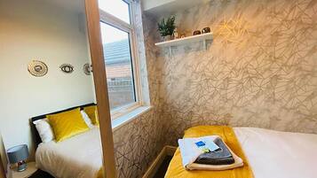 A hotel room with two beds, a window, a geometric-patterned wall, and a shelf with decorative items.