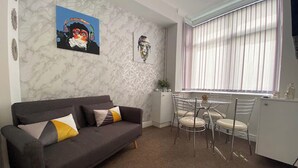A modern living room with a grey sofa, a dining table with chairs, and a window with blinds. - Townhouse @ 110 Etruria Vale Road Stoke (Stoke-on-Trent)