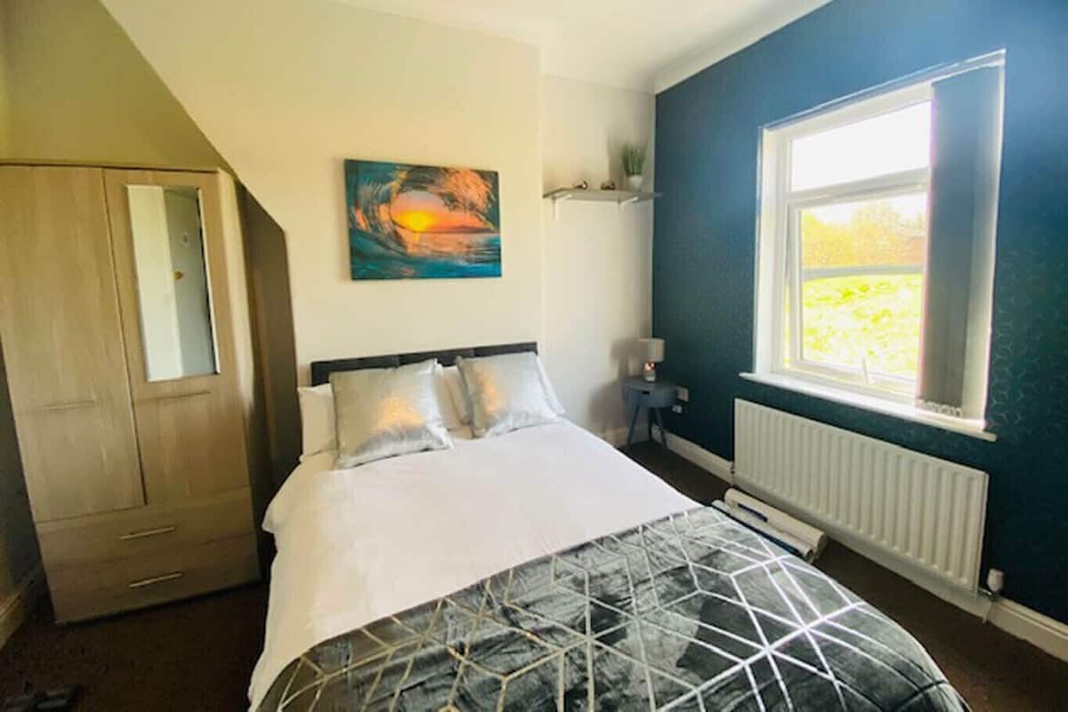 Un dormitorio con cama, un cuadro, una ventana y un radiador.