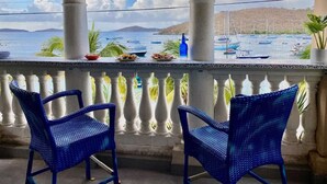 Un balcon avec deux fauteuils en osier bleu, une balustrade blanche et une vue sur les bateaux qui naviguent sur l’eau.
