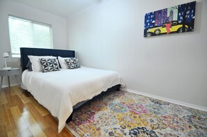 A bedroom with a bed, a nightstand, a window with blinds, and a colorful rug.