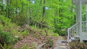 A house with a porch, surrounded by a forested area with a stone pathway leading to the entrance. - Mountaintop suite, mountain views, one level, King bed, pet friendly, accessible (Rosman)