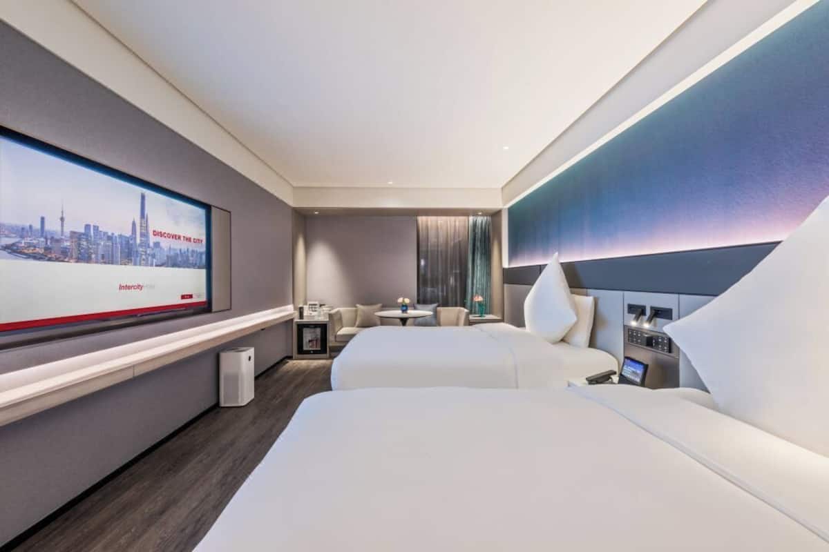 A modern hotel room with a large bed, a desk, and a television displaying a cityscape.