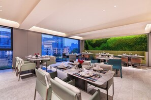 Un restaurant moderne doté de plusieurs espaces de restauration, de grandes fenêtres et d’un mur végétal.