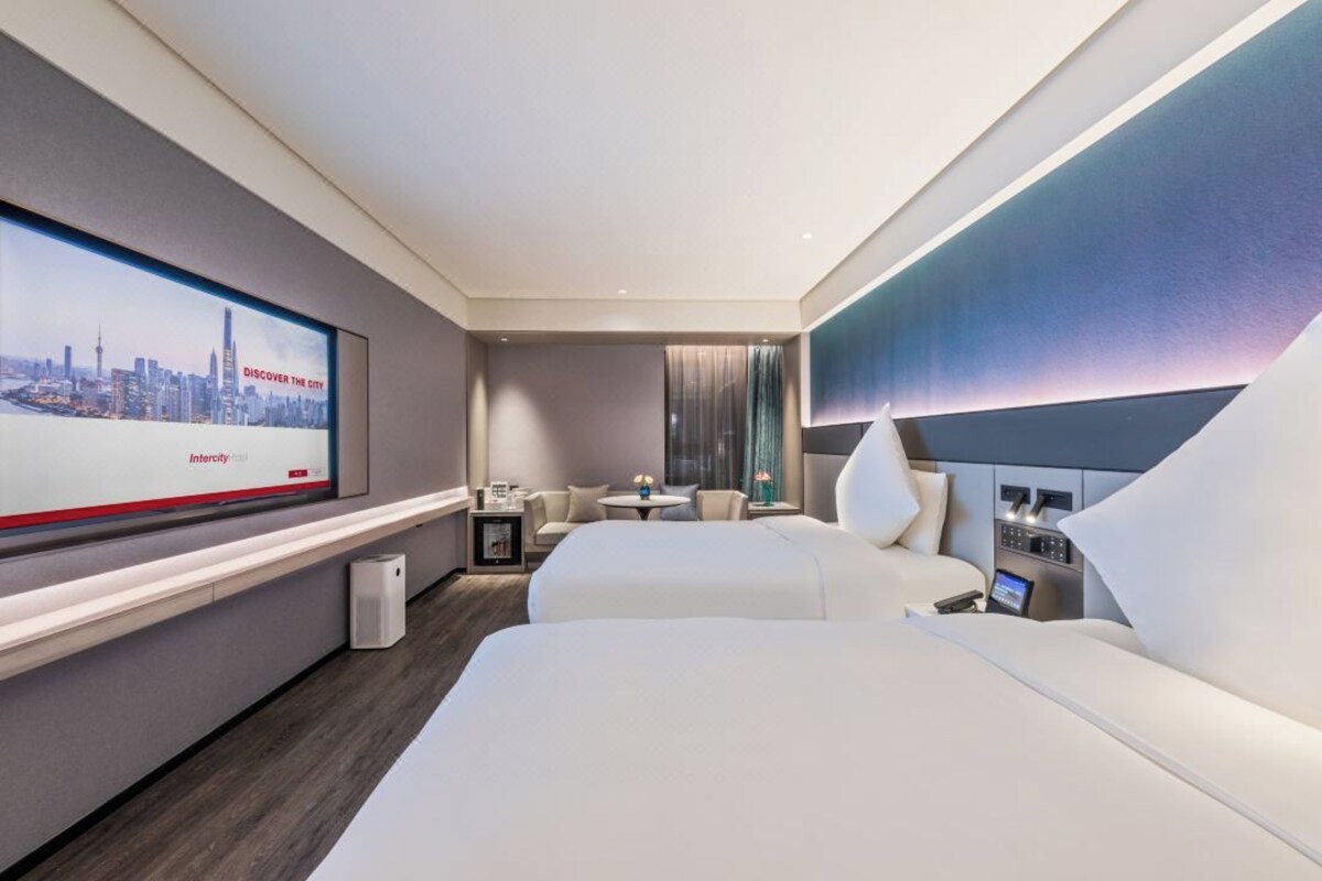 Una habitación de hotel moderna con una cama grande, un escritorio y un televisor que muestra un paisaje urbano.