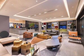 Un hall d’hôtel moderne avec un comptoir d’accueil, des espaces détente et une grande fenêtre.