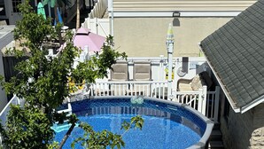 Un jardin avec une piscine, des chaises vertes et une petite table.