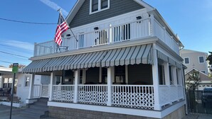 Une maison à deux étages avec un balcon, une véranda dotée d’un auvent à rayures et un drapeau américain.