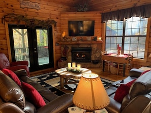 A cozy cabin interior with a fireplace, leather sofas, a TV, and a dining table with candles.