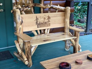 A rustic wooden bench with a 'WELCOME' sign, placed on a wooden deck with a table and coasters nearby.