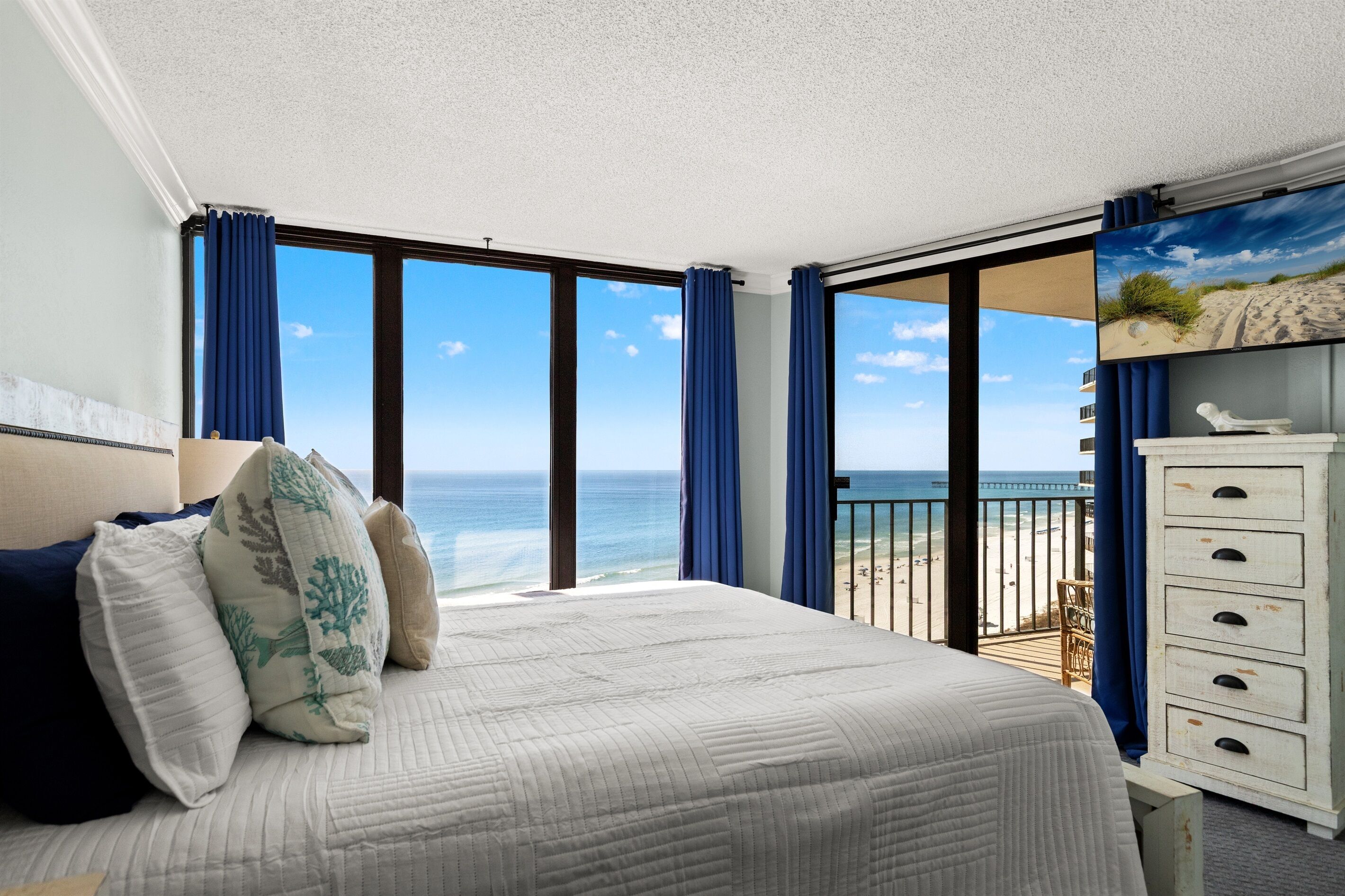 Un dormitorio con una cama grande, un aparador y vistas a la playa y al océano.