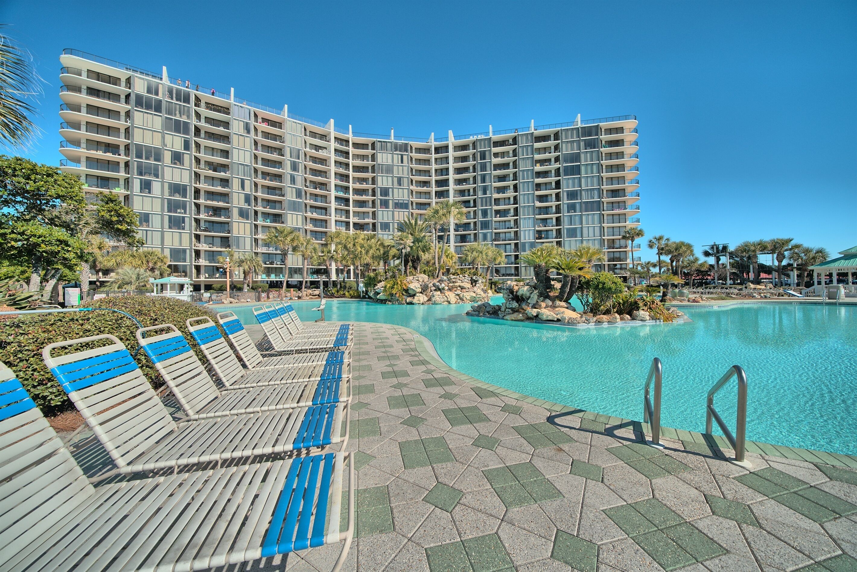 A hotel with a large pool area, lounge chairs, and a clear view of the building's exterior.