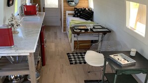 Una kitchenette compacta y moderna con suelo de madera, una pequeña mesa de comedor y una cama con un espejo sobre ella.