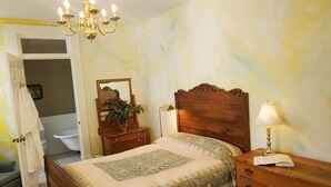 A bedroom with a wooden bed, a nightstand with a lamp, a dresser, a mirror, and a chandelier. - Vintage Q ensuite room, historic railroad hotel (Cowan)