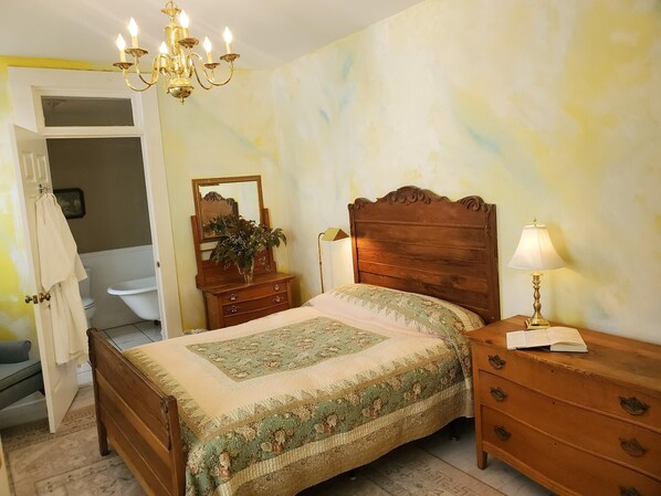 A bedroom with a wooden bed, a nightstand with a lamp, a dresser, a mirror, and a chandelier.
