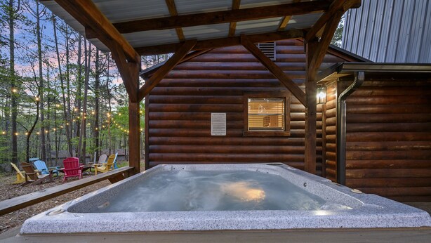 A log cabin with a hot tub, wooden deck, and Adirondack chairs.