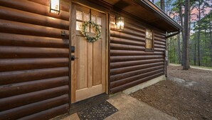 A log cabin with a wooden door, a wreath, and two exterior lights.