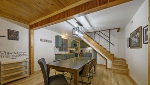 A dining area with a wooden table and chairs, a staircase leading to a kitchen, and a sign on the wall.
