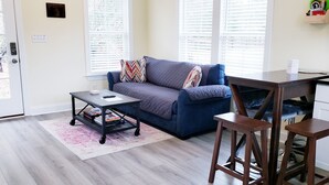 A modern living room with a blue sofa, a coffee table, and a wooden desk. - Mulberry Cottage on 16 Acres, King Size Bed, No Pet Fee (Grovetown)