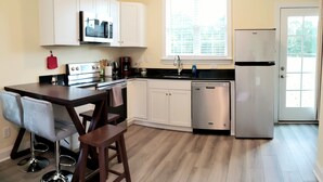 A modern kitchen with white cabinets, a black countertop, and a stainless steel dishwasher. - Mulberry Cottage on 16 Acres, King Size Bed, No Pet Fee (Grovetown)