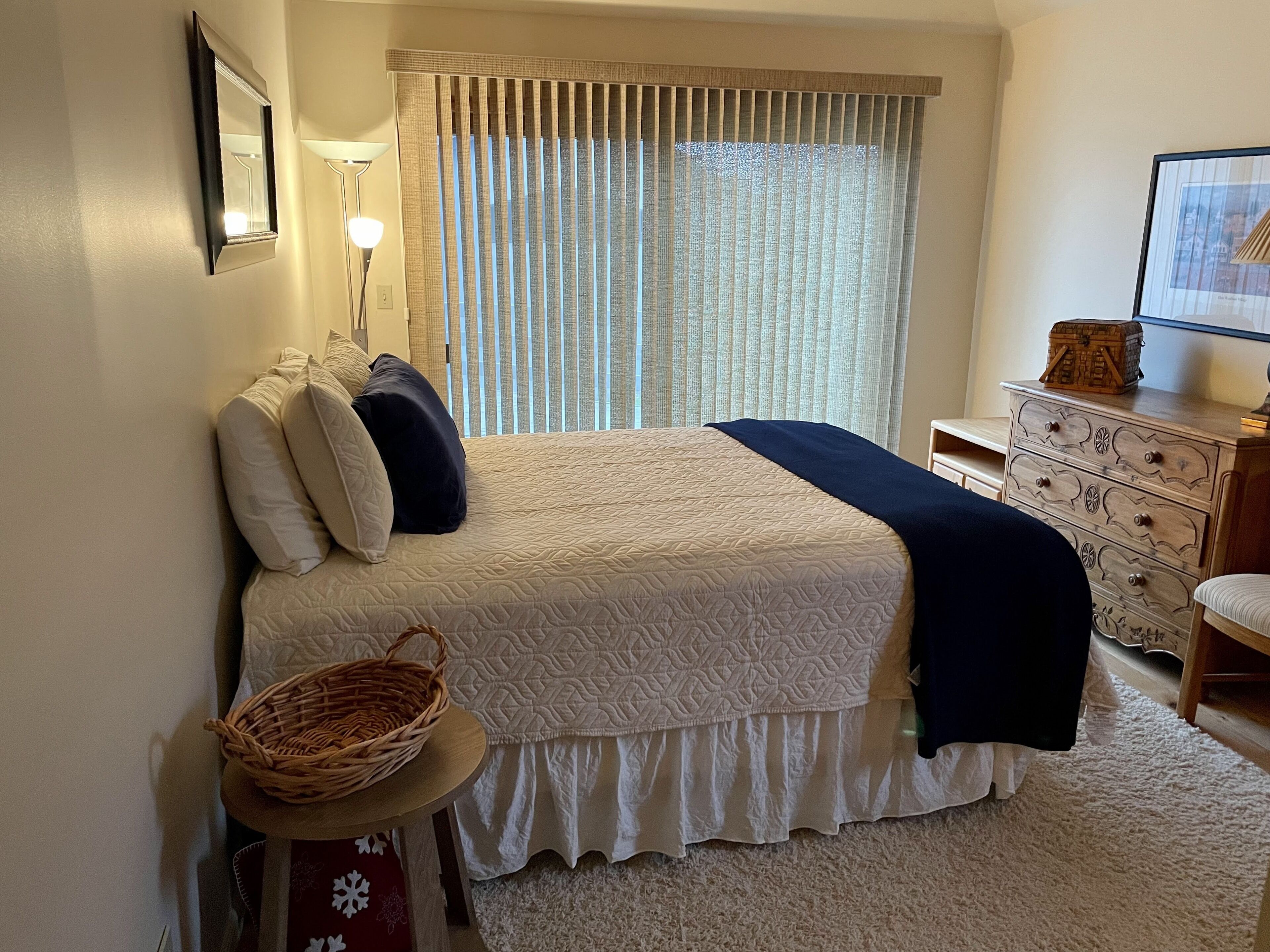 Un dormitorio con cama, mesita de noche, lámpara, cómoda y cortinas.