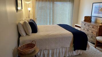 Un dormitorio con cama, mesita de noche, lámpara, cómoda y cortinas.