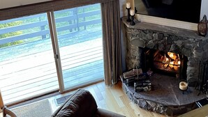 Un saló acollidor amb una llar de pedra, un televisor de pantalla plana gran penjat a la paret i una zona de seients confortable amb un sofà i butaques.