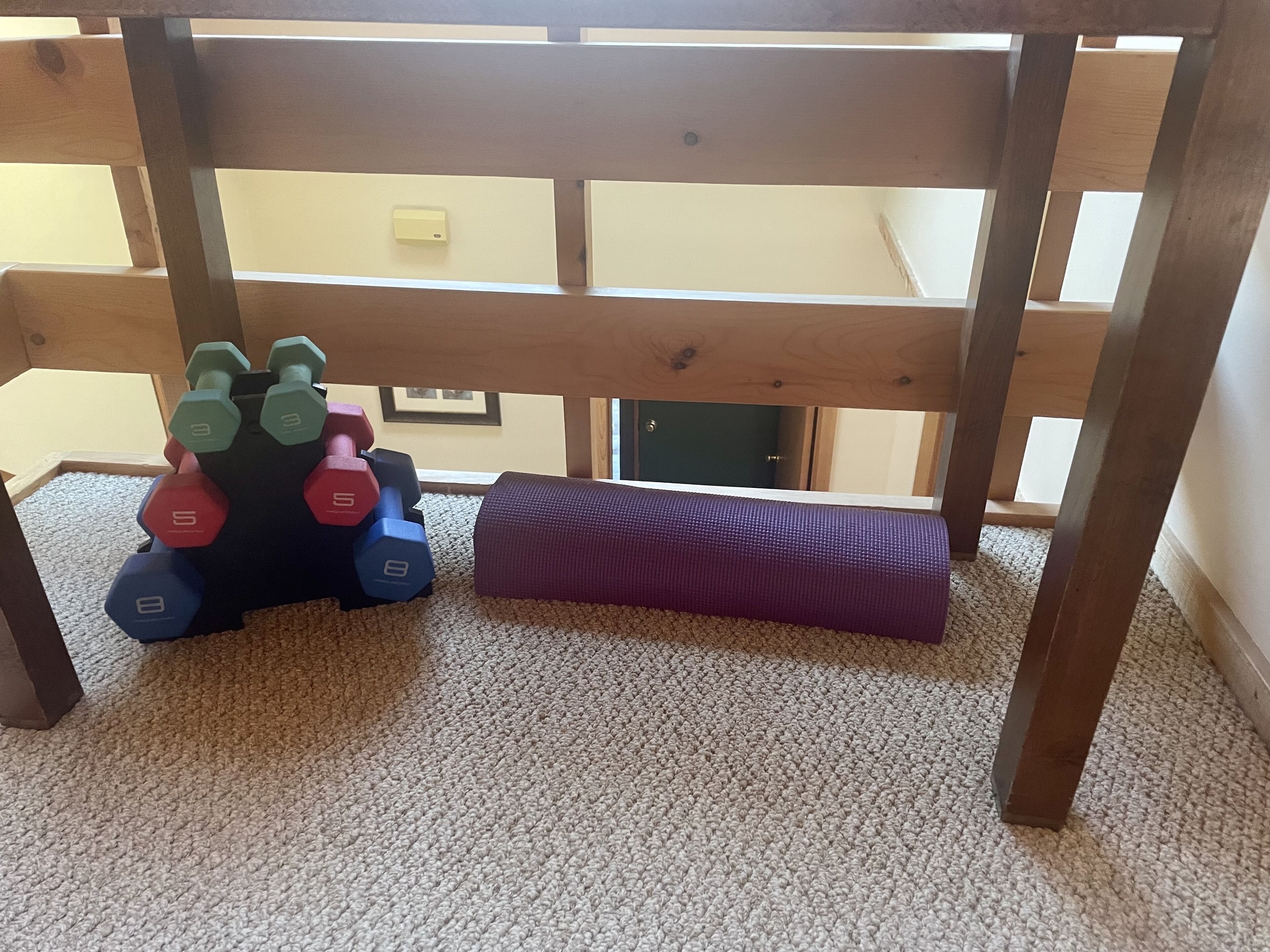 A wooden table with a carpeted floor, a purple exercise mat, and a set of dumbbells.
