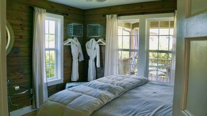 A bedroom with a large bed, wooden walls, and a balcony with outdoor furniture. - Molly Cabin  - Private cabin with 2 bedrooms, one queen and one king bed, full bath with walk-n-shower. Full kitchen with fridge/ice maker, coffee bar, front and back porches, private out door fire pit, outdoor shower. (Round Top)
