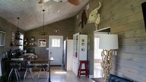 A rustic kitchen with wooden walls, a ceiling fan, and a cow skull decoration. - Molly Cabin  - Private cabin with 2 bedrooms, one queen and one king bed, full bath with walk-n-shower. Full kitchen with fridge/ice maker, coffee bar, front and back porches, private out door fire pit, outdoor shower. (Round Top)