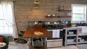 A rustic kitchen with wooden walls, a wooden table, and a stove. - Molly Cabin  - Private cabin with 2 bedrooms, one queen and one king bed, full bath with walk-n-shower. Full kitchen with fridge/ice maker, coffee bar, front and back porches, private out door fire pit, outdoor shower. (Round Top)
