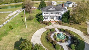 A large two-story house with a front porch, a circular driveway, and a small pond. - 2-bedroom Barn 1-bathroom Apartment Sleeps 7  (Parkton)