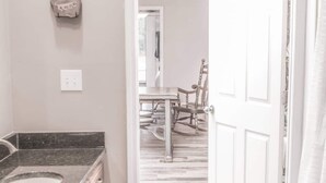 A bathroom with a granite countertop sink, wooden cabinets, and a white door leading to a dining area with a wooden table and chairs. - 2-bedroom Barn 1-bathroom Apartment Sleeps 7  (Parkton)