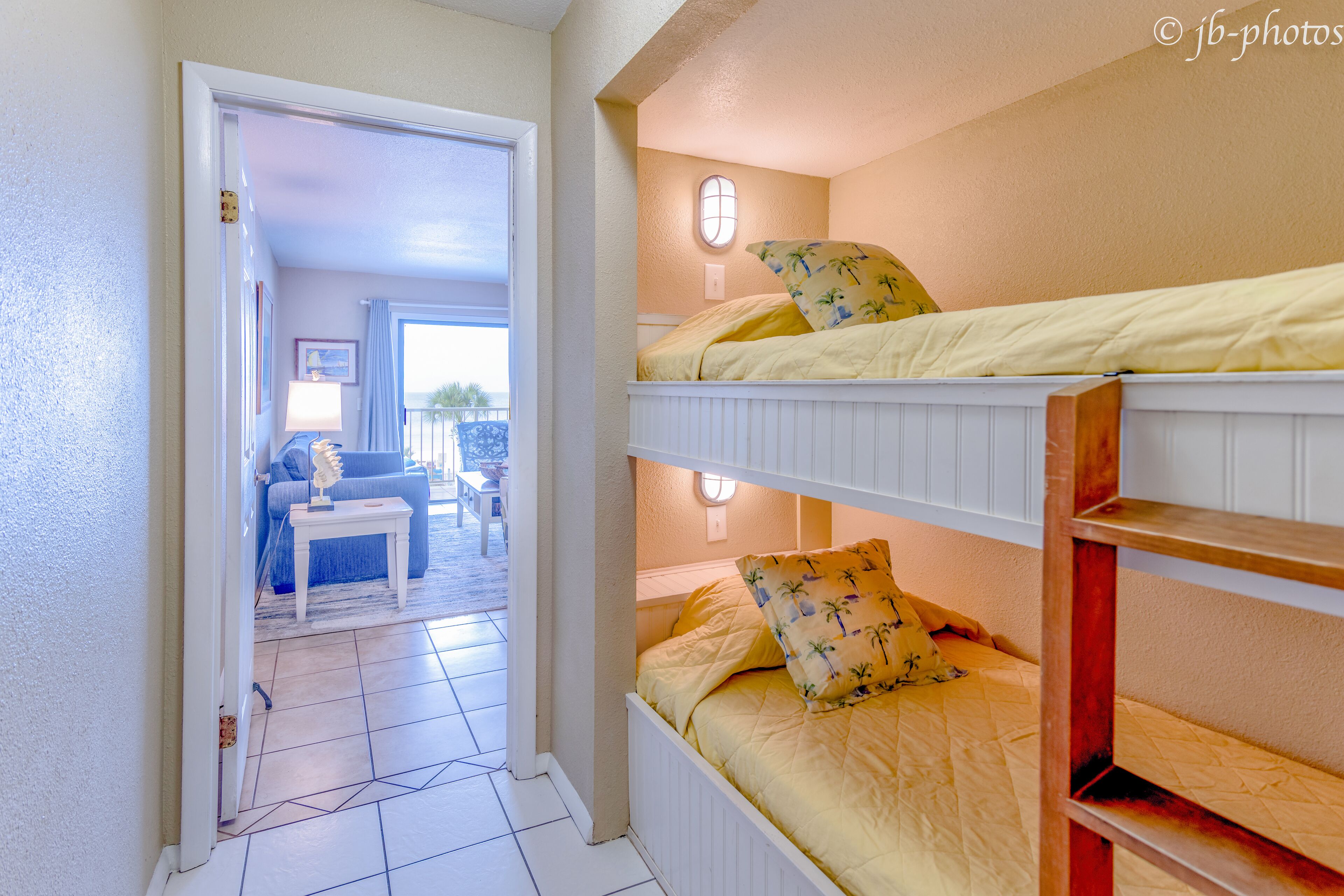 A room with bunk beds, a door leading to a living area, and a window with a view.