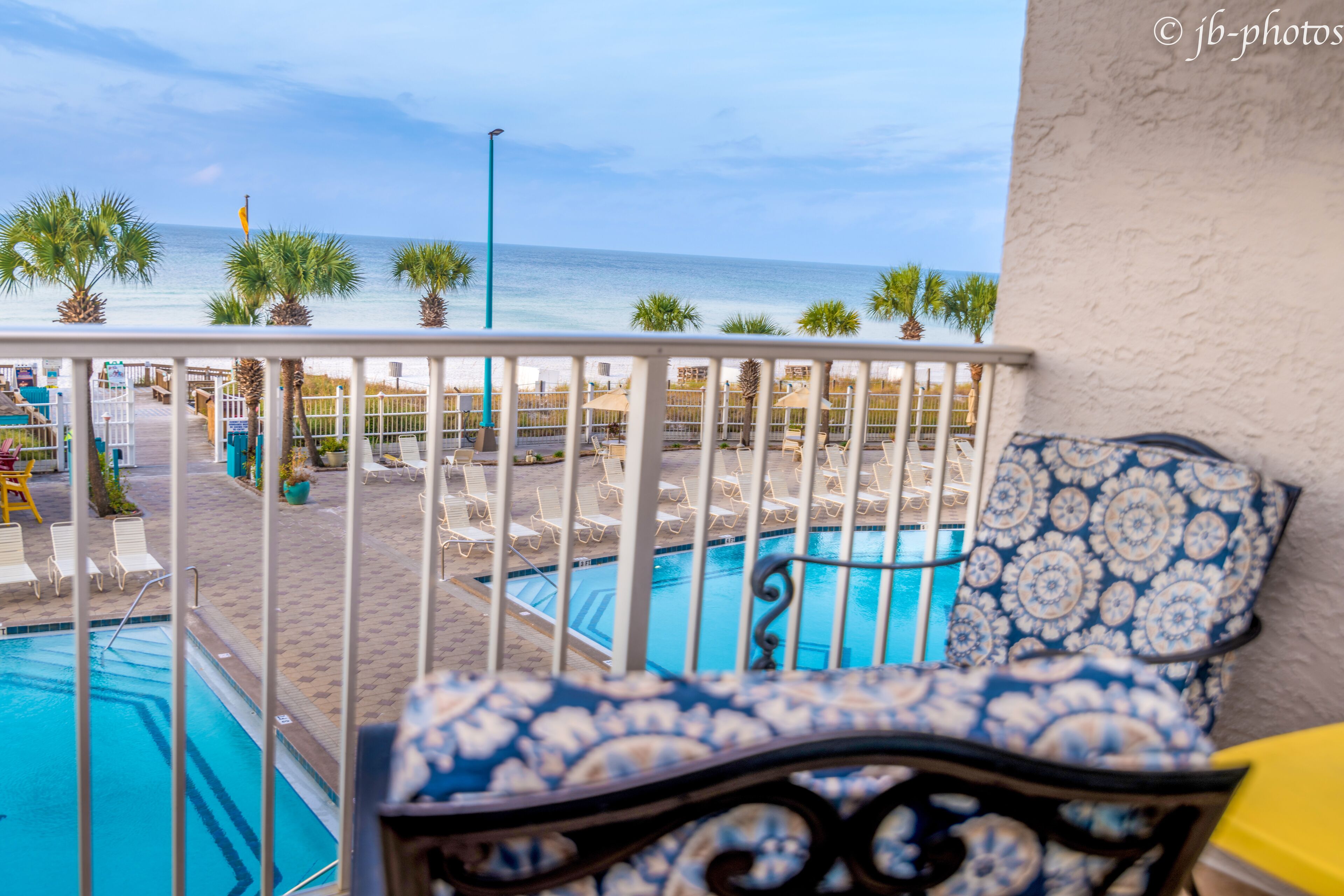A poolside area with a view of the ocean, a pool, and a seating area with a patterned chair.