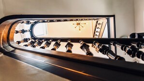 Un escalier moderne à la surface réfléchissante, menant à une pièce agrémentée d’un lustre et d’une fenêtre.