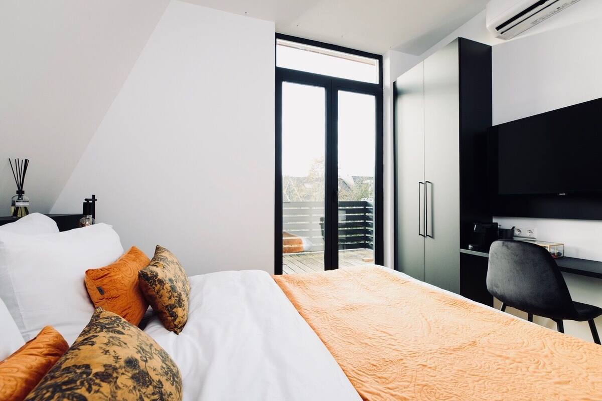 Ein modernes Hotelzimmer mit Bett, Schreibtisch, Fernseher und einem Balkon mit Aussicht.