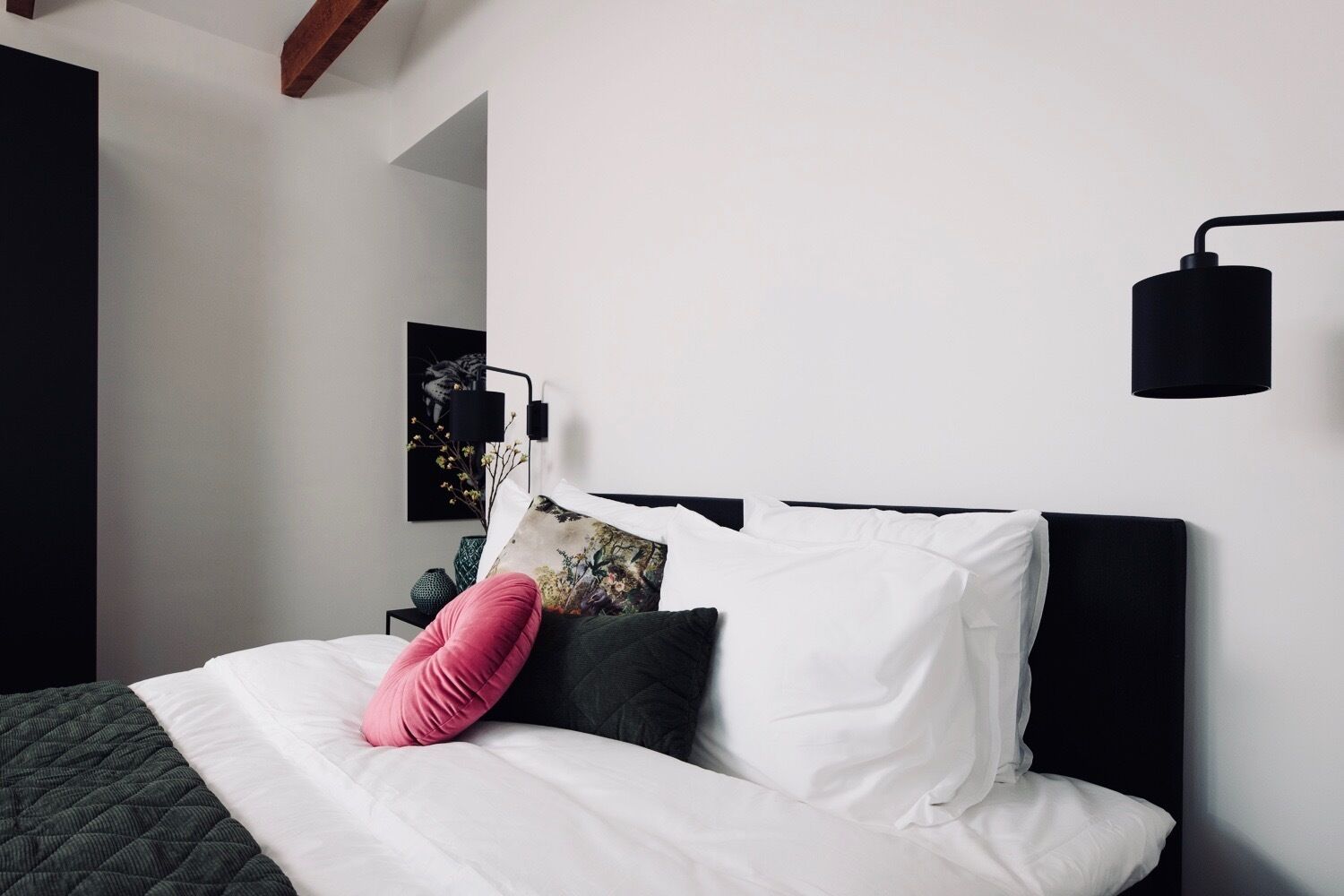 A modern bedroom with a bed, a black wall-mounted lamp, and a framed picture on the wall.