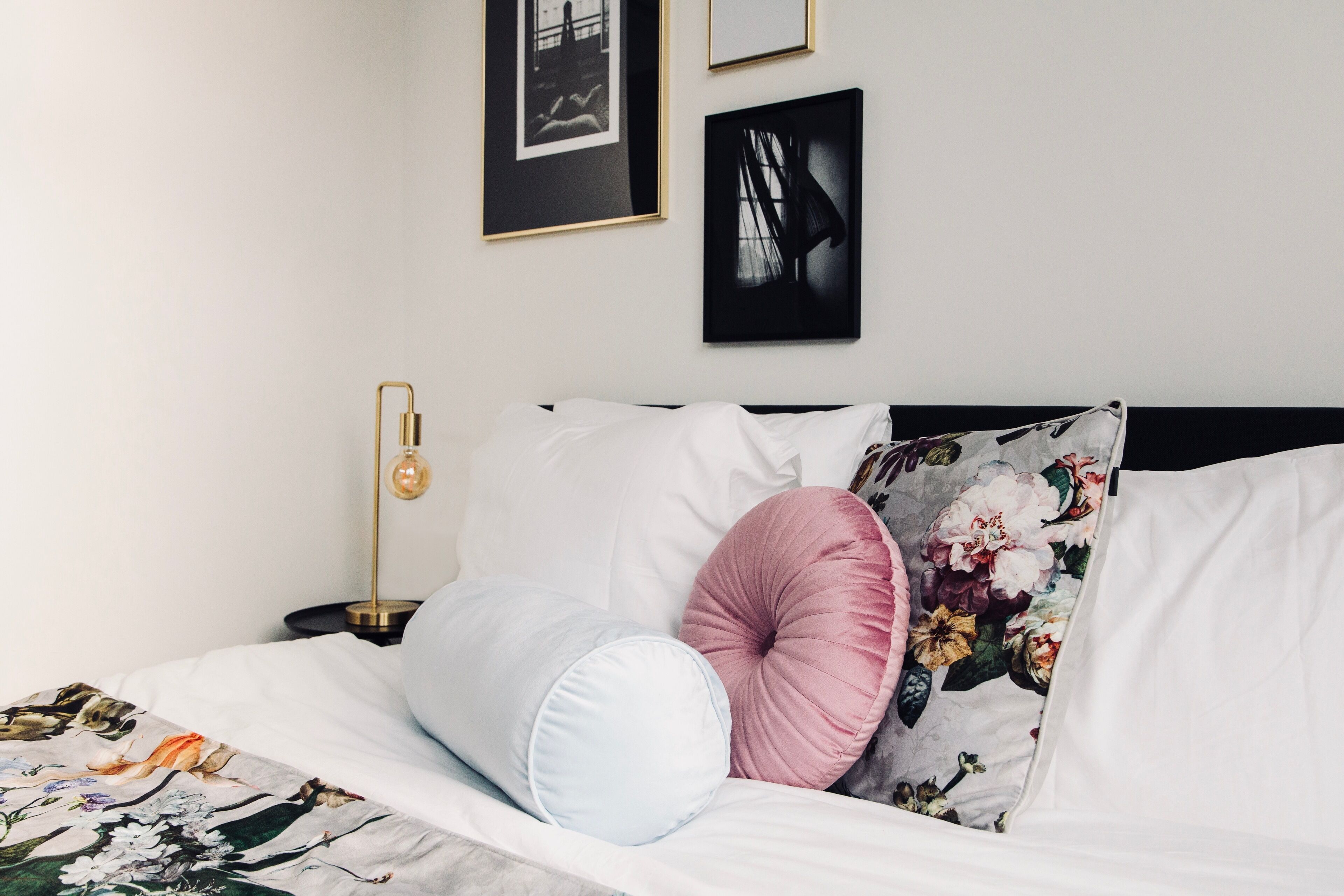 A neatly made bed with floral bedding, a black headboard, and a bedside table with a lamp.