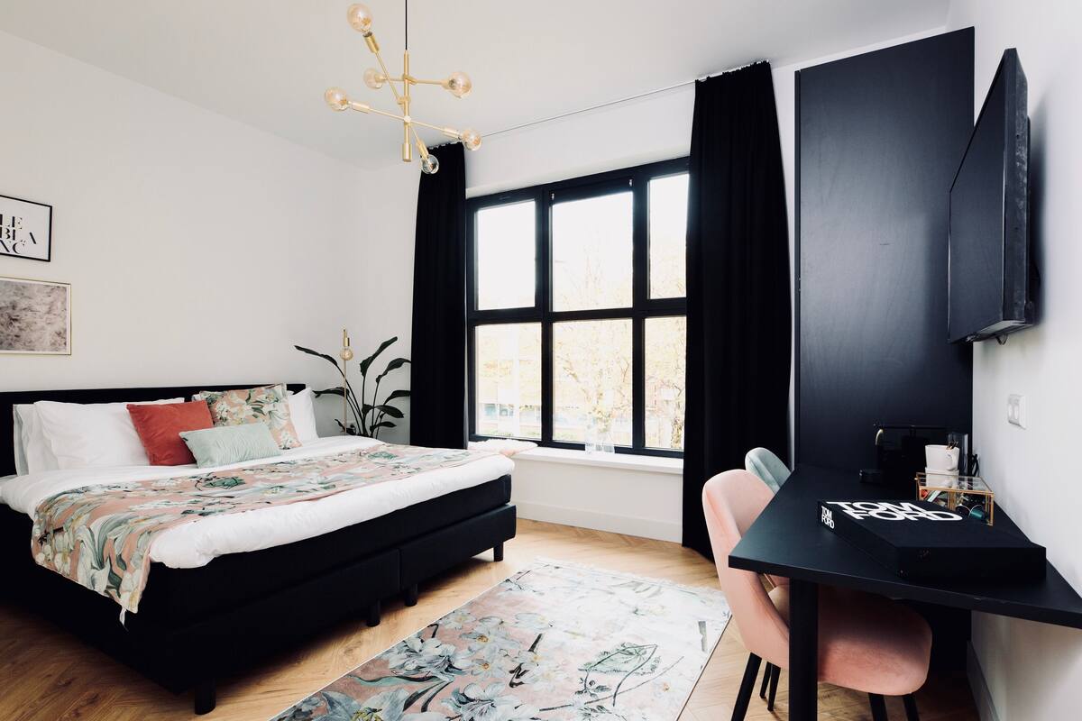 Ein Schlafzimmer mit Bett, Schreibtisch, Stuhl, Fernseher und Fenster.