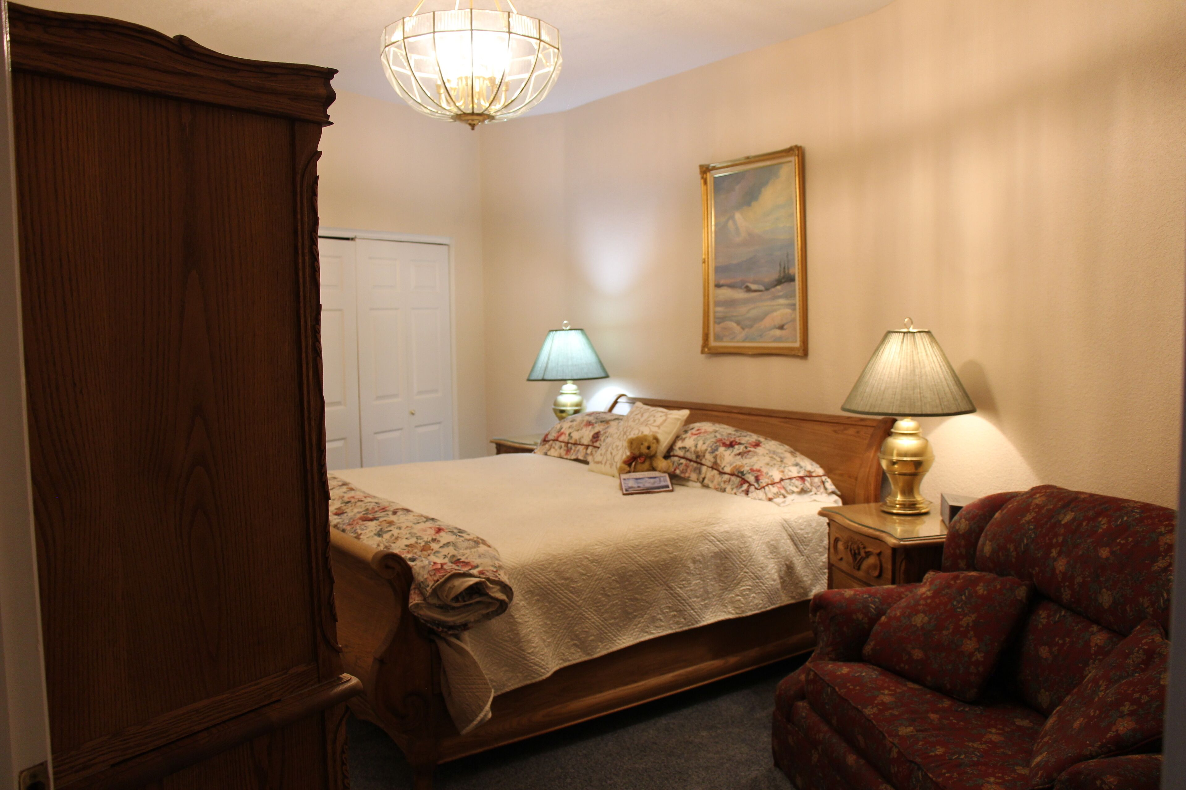 A bedroom with a bed, a nightstand, a lamp, a chair, and a door.
