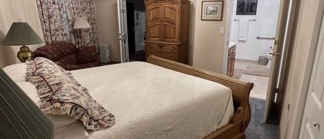 A bedroom with a large bed, a wooden wardrobe, a nightstand, a lamp, and a ceiling light fixture.