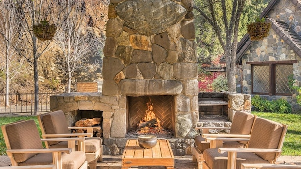 A stone fireplace with a fire, surrounded by wooden furniture and a stone wall.