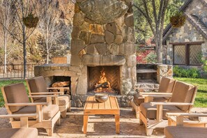 A stone fireplace with a fire, surrounded by wooden furniture and a stone wall. - Calistoga Creek Side Mountain Estate (Middletown)