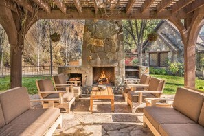 Une cheminée en pierre, entourée de meubles en bois, se trouve dans un espace patio extérieur.