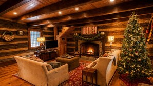 Ein Holzblockhaus-Interieur mit Kamin, zwei Sofas, einem Weihnachtsbaum und einem Fernseher.
