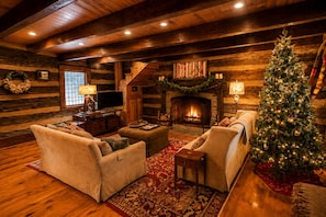Een houten chalet interieur met een open haard, twee banken, een kerstboom en een televisie.