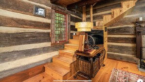 Ein Blockhaus-Interieur mit Holzwänden, einer Treppe, einem Holzwagen und einem Fenster mit Gittermuster.
