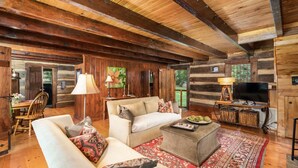 Ein Holzblockhaus-Interieur mit Holzbalkendecke, einer Couch, einem Couchtisch und einem Fernseher.